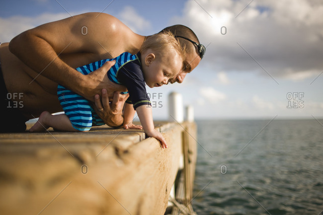 Father helping his baby son pier over the edge of a pier