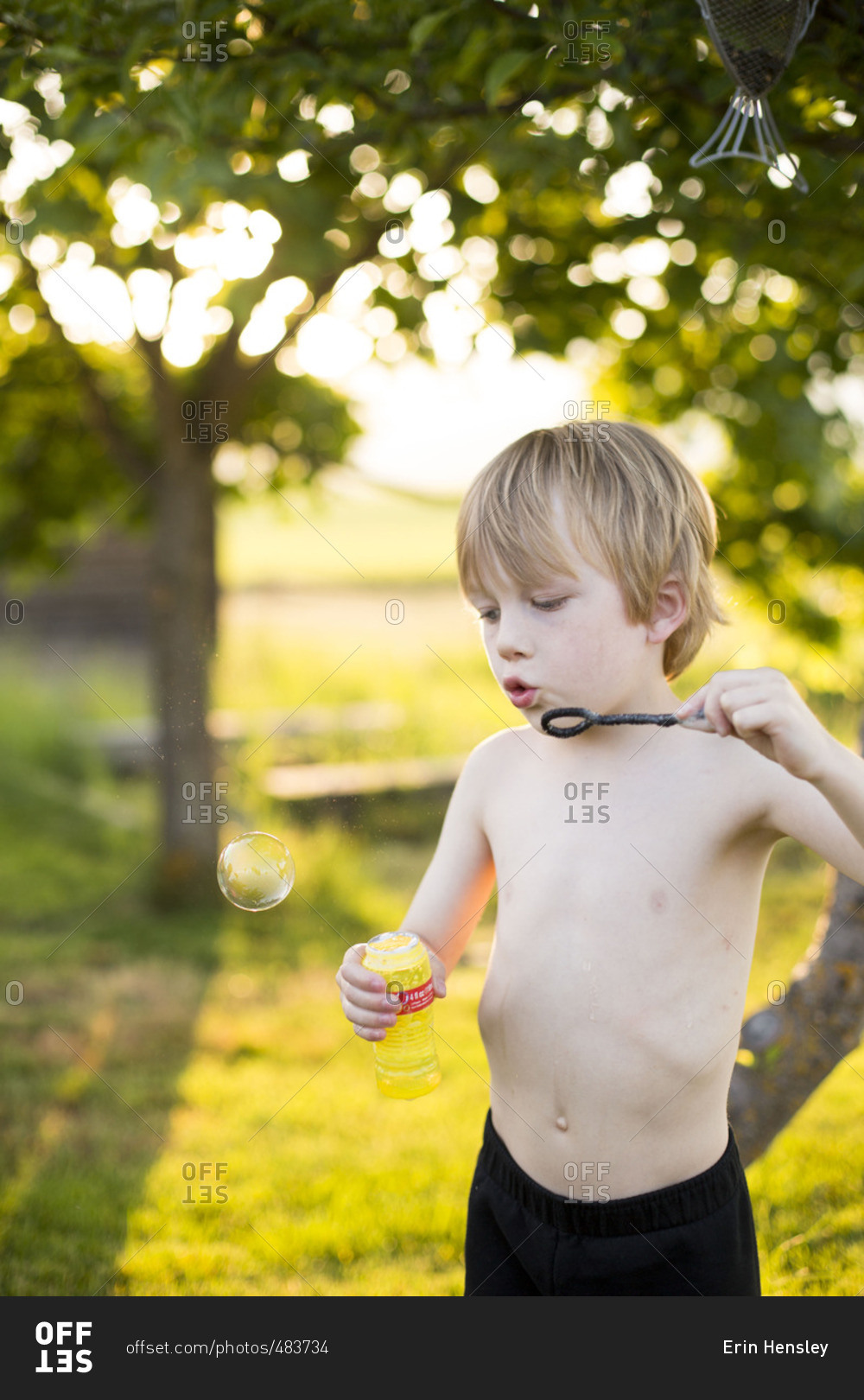 Shirtless boy blowing bubbles in backyard at dusk stock photo - OFFSET