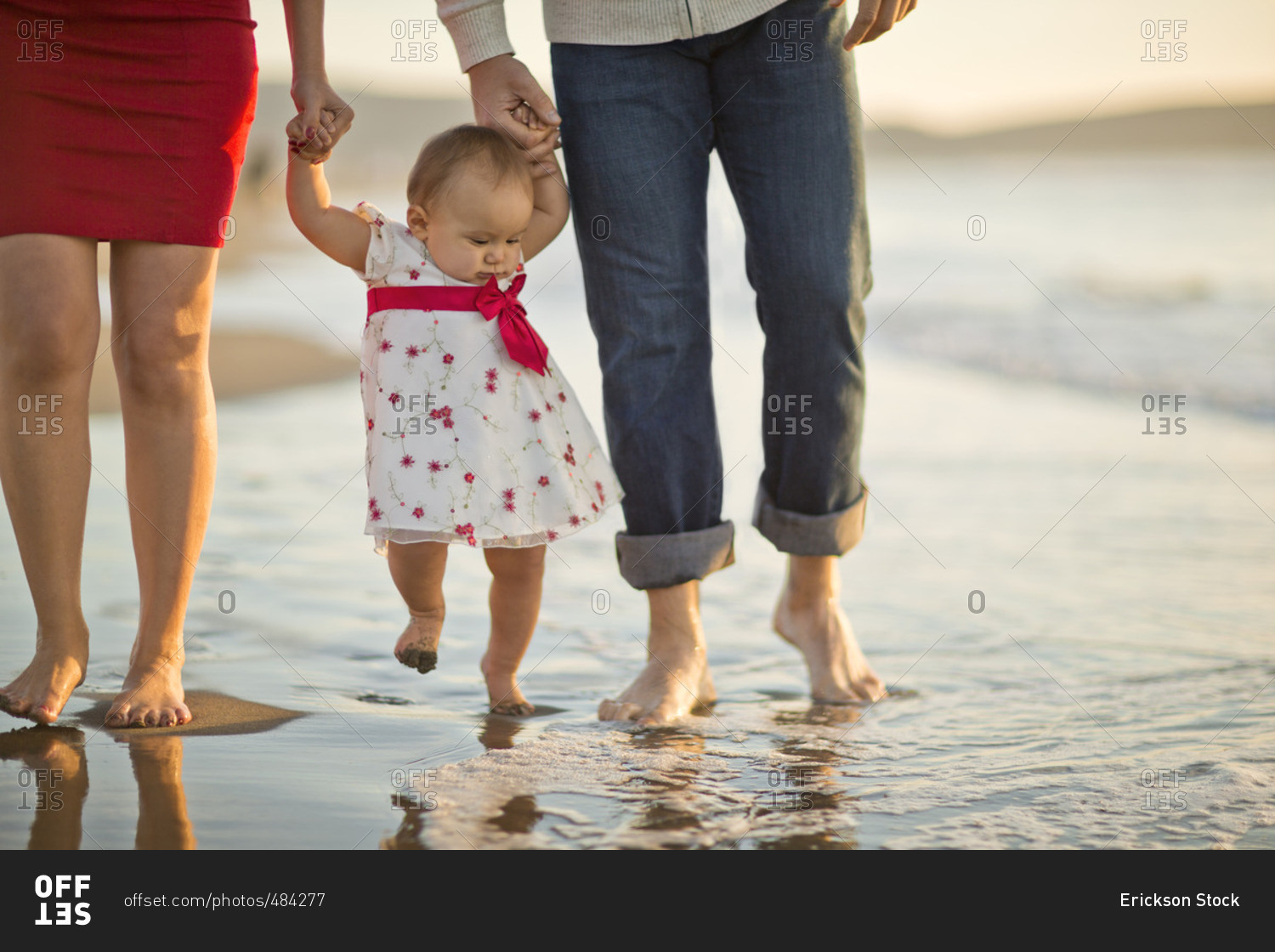 Parents walking with their baby girl on the beach.