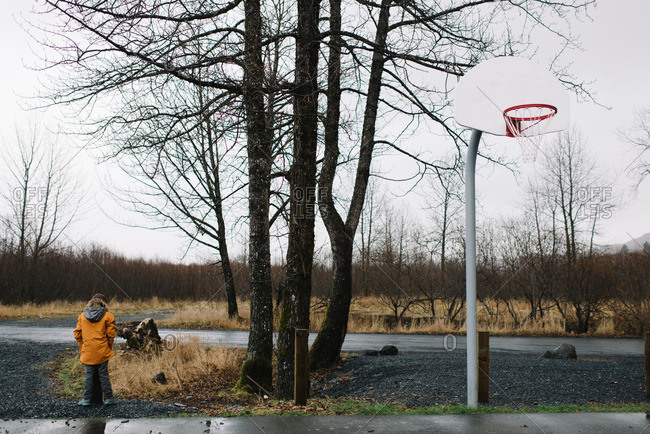 Boy standing at edge of basketball court in rainy weather