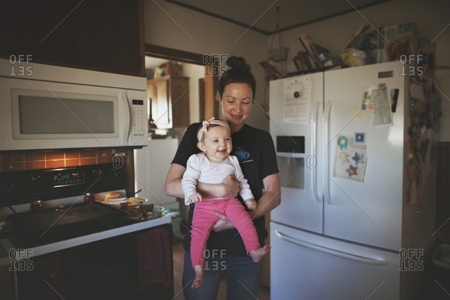 Mom holding grinning girl in kitchen