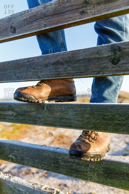 Person wearing boots and jeans climbing on a wooden fence