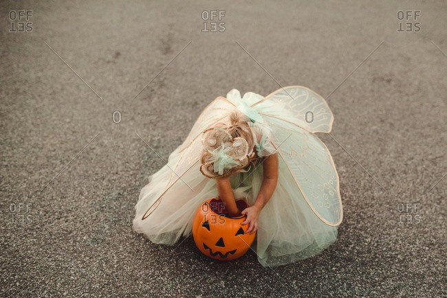 Little girl dressed as a fairy for Halloween looking through her bucket