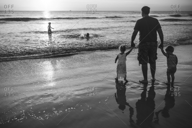 Father walking with toddlers in the ocean in black and white
