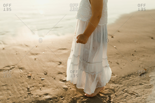 Little girl standing barefoot in a white dress on a beach