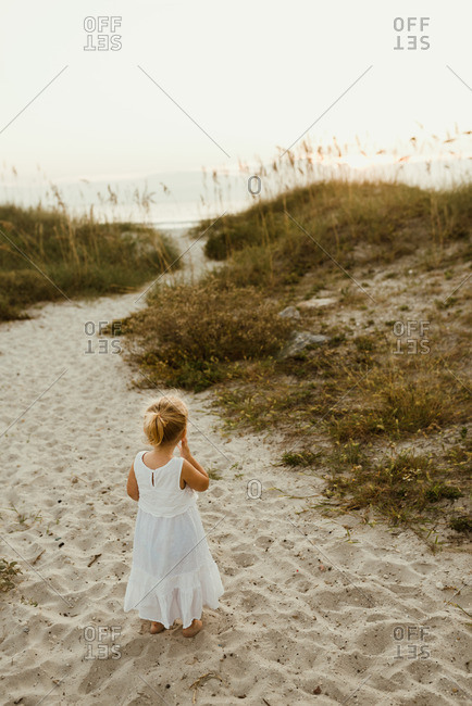 Little blonde girl standing in the sand in a white dress