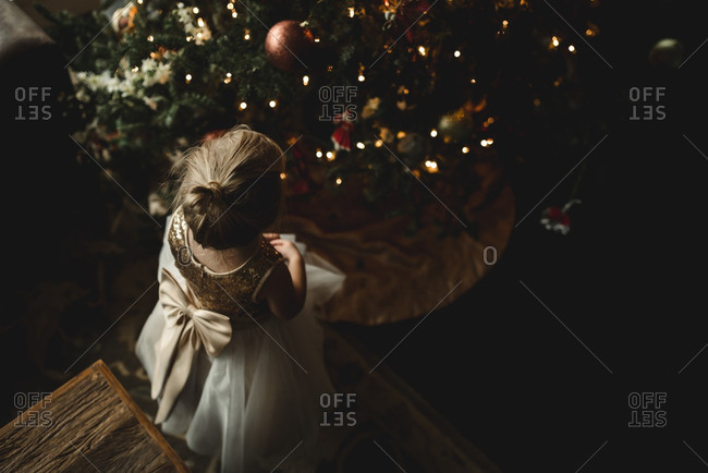 Little girl in a dress looking at a Christmas tree