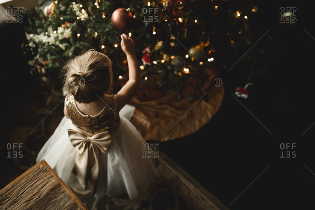 Little girl in a dress touching ornaments on a Christmas tree