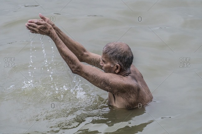 Varanasi, India - July 8, 2016: A Hindu man bathes and prays in the Ganges River, Varanasi