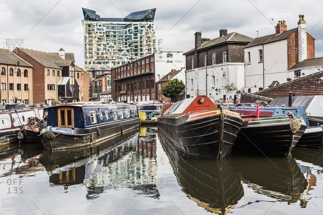 Birmingham, England - July 12, 2014: Gas Street Basin area (a canal basin in the center of the town), typical boats in a canal, The Cube building on the background