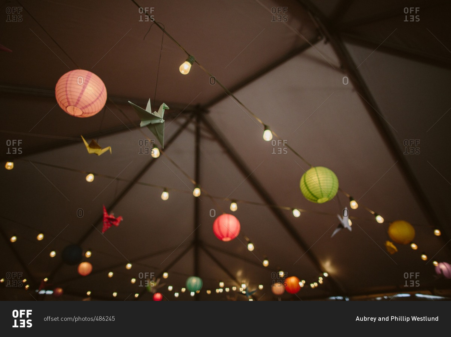 Origami birds and paper lanterns hanging from strung lights outside at night