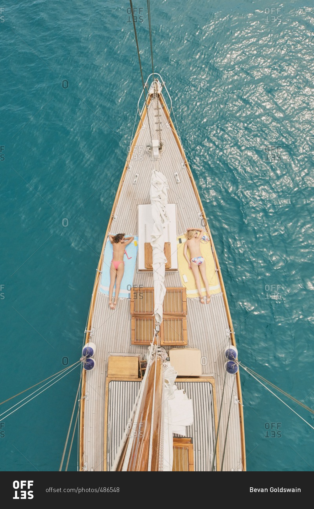 Beautiful girl friends tanning on sailboat in ocean from overhead