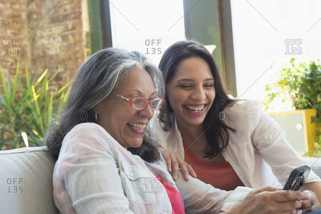 Hispanic women sitting on sofa texting on cell phone