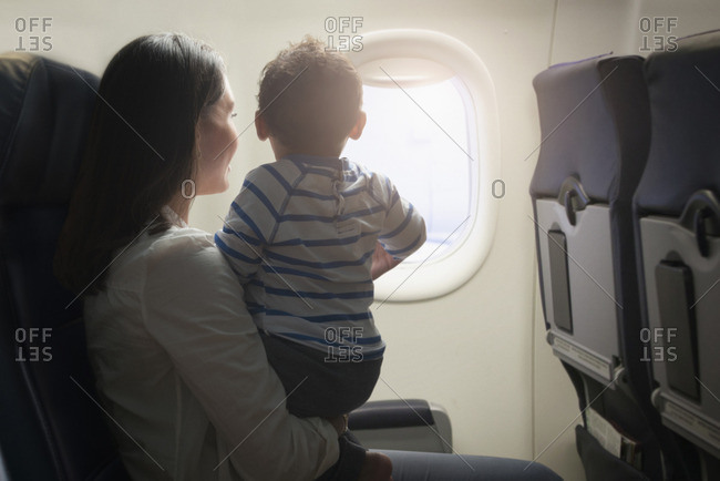 Hispanic mother and son sitting in airplane near window