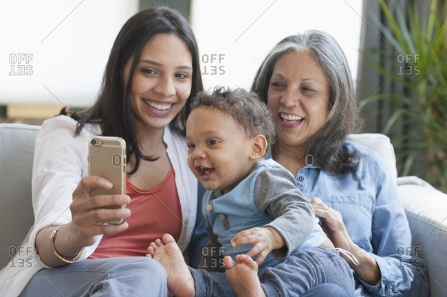 Hispanic mother and grandmother posing for cell phone selfie with baby boy