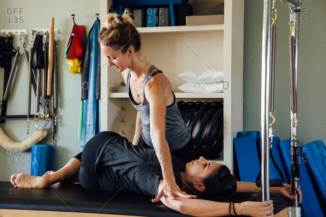 A 20-year-old female trainer practices Pilates on an elevator chair,  lifting her leg high above her head. A woman rests on her knee and hands  Stock Photo - Alamy