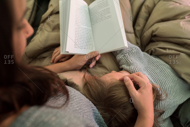 Young girl sleeping on her mother, while her mother reads a book, rear view