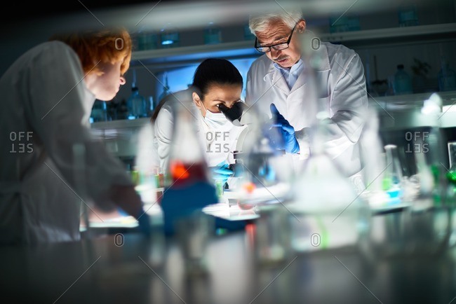 Confident scientists in white coats standing at the table with laboratory glassware