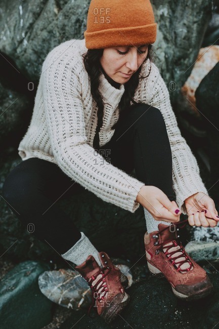 Woman tying her hiking boots while seated on rocks