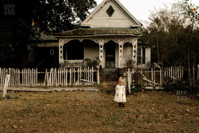 Toddler girl with blonde hair in front of an old country house