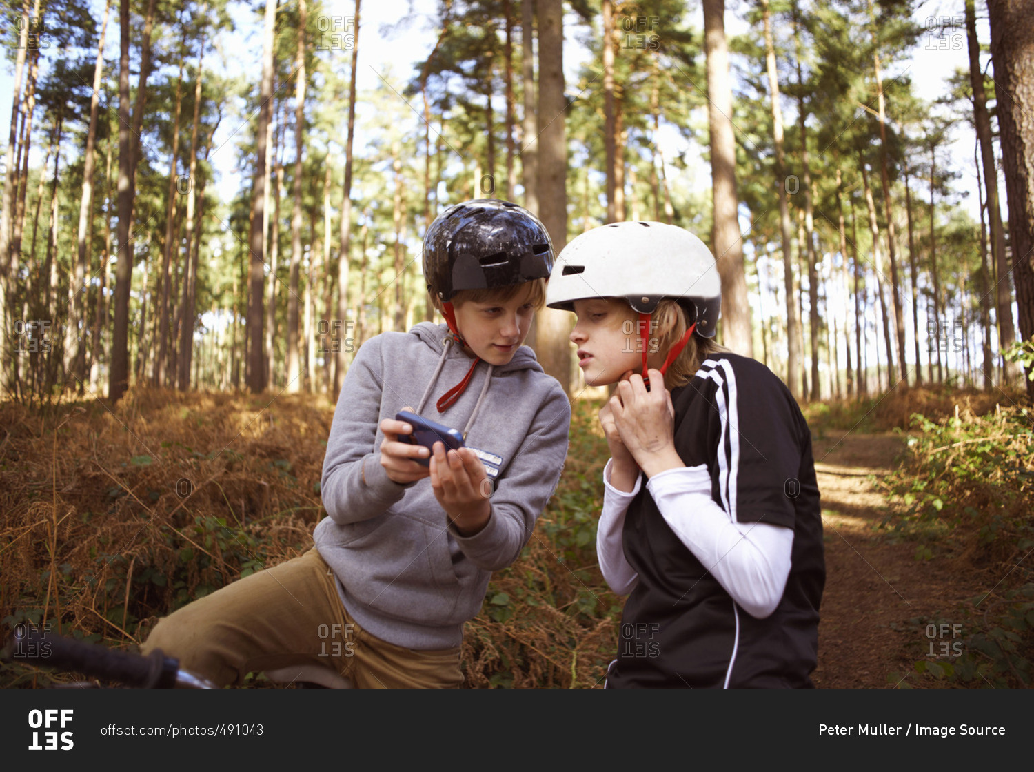 Twin brothers on bikes in forest looking at smartphone