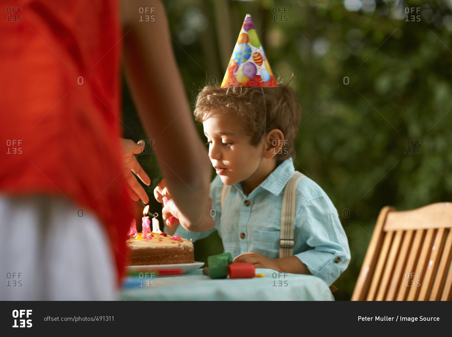 Mother with son blowing candles on birthday cake at garden birthday party