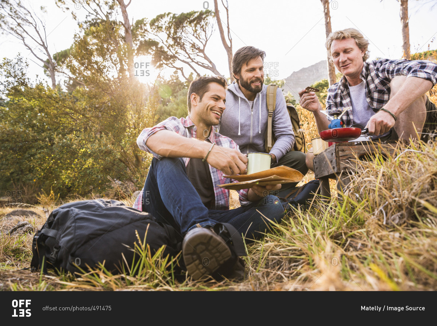 Three men frying breakfast on camping stove in forest, Deer Park, Cape Town, South Africa