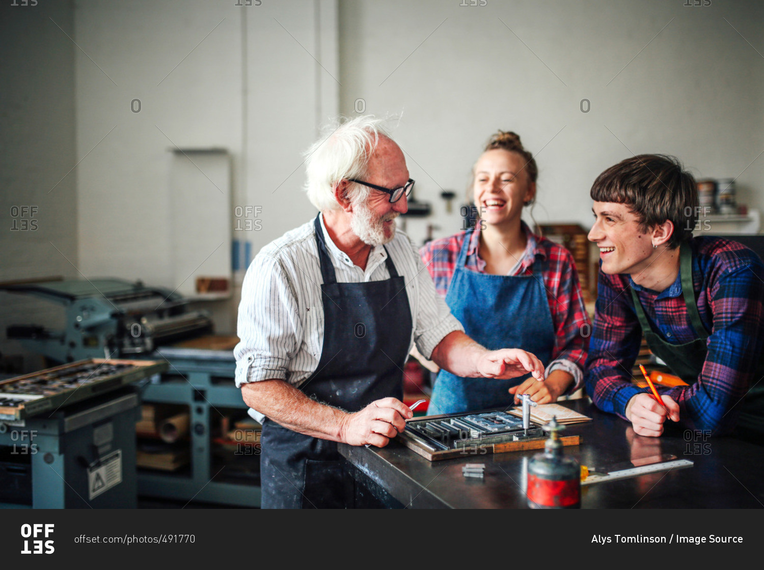 Senior craftsman laughing with young craftsman and craftswoman in letterpress workshop