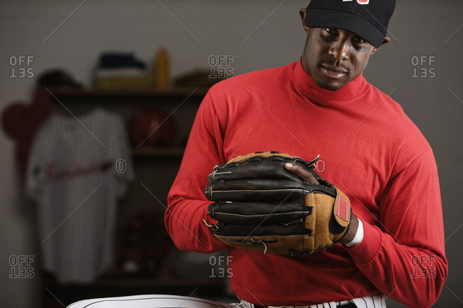 African baseball player holding glove in locker room