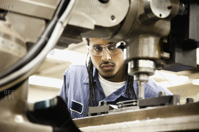 Hispanic man using machine in machine shop