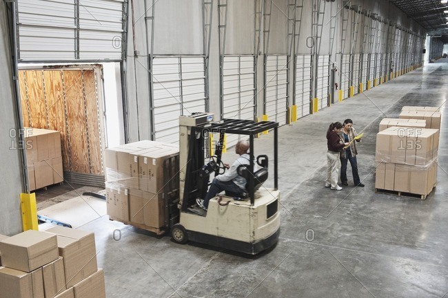 Forklift moving boxes onto truck at loading dock of warehouse