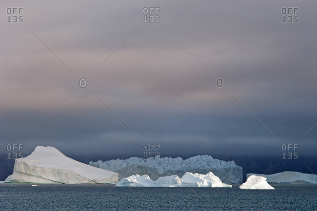 Sunset sky, with heavy cloud and floating icebergs with smooth eroded shapes on the waters of Baffin Island.