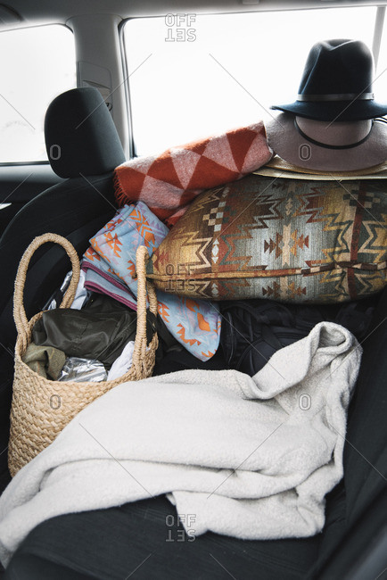Close up of items on the back seat of a car, cushions, hats and a bag and blanket.
