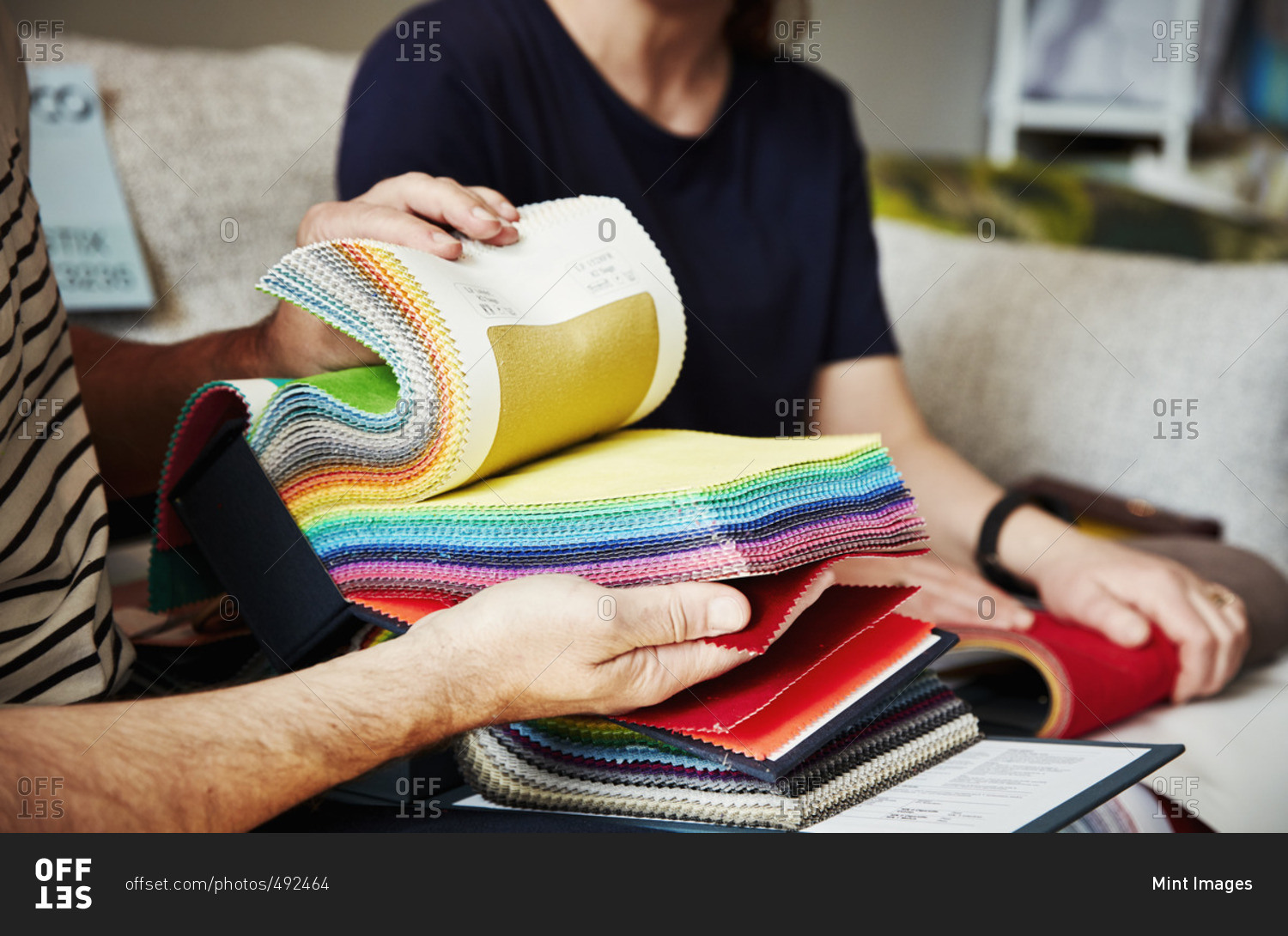 Two people sitting on a sofa, looking at a selection of fabric samples.