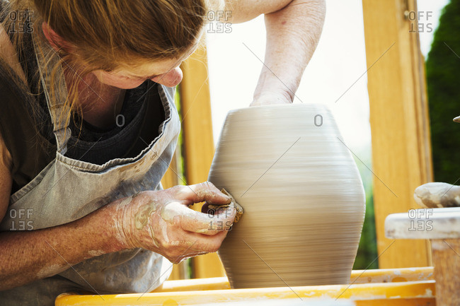 A woman potter working clay on a potter's wheel in her workshop.