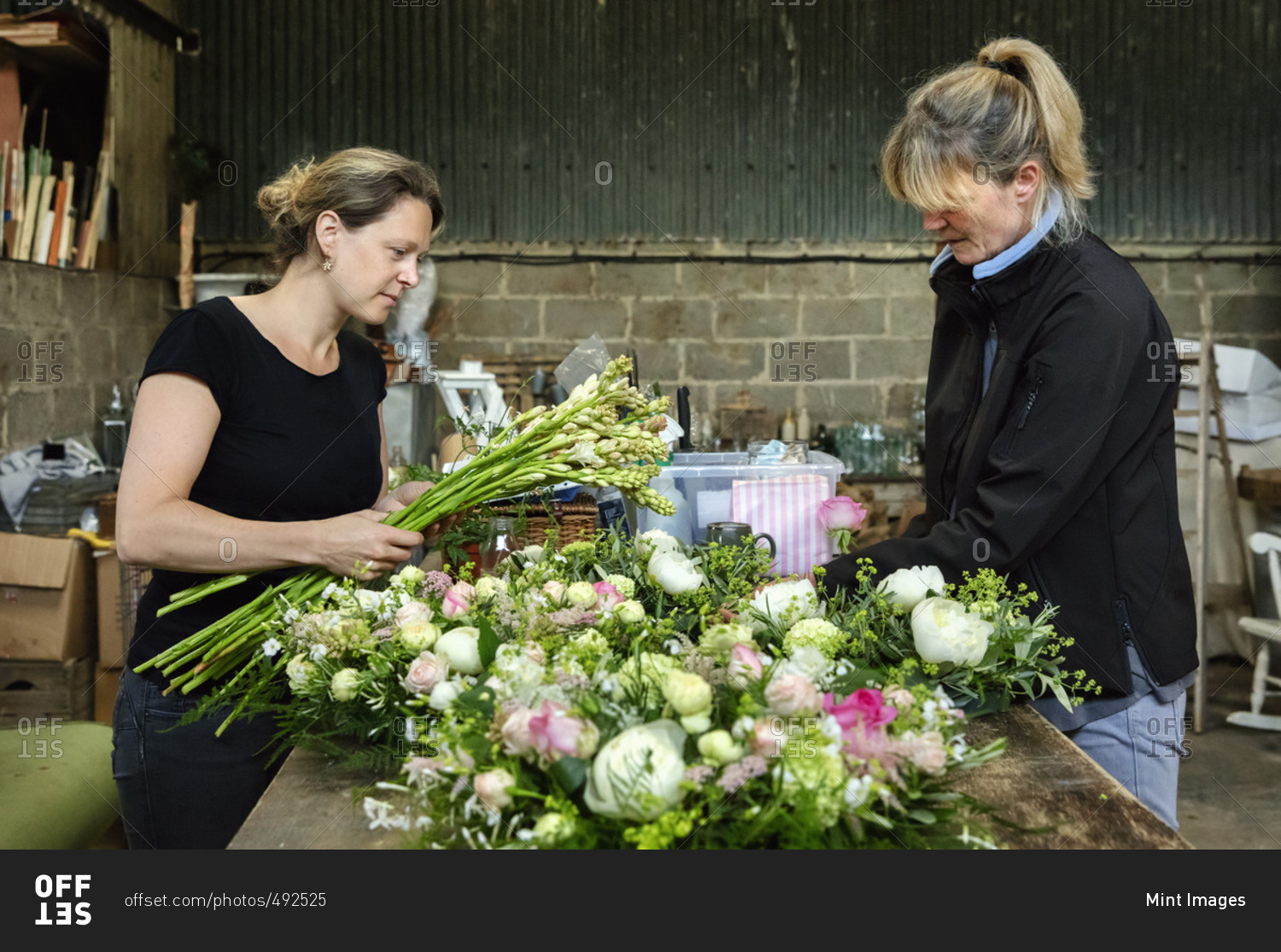 Commercial flower arranging. Two women at a workbench creating floral table decorations and arrangements.