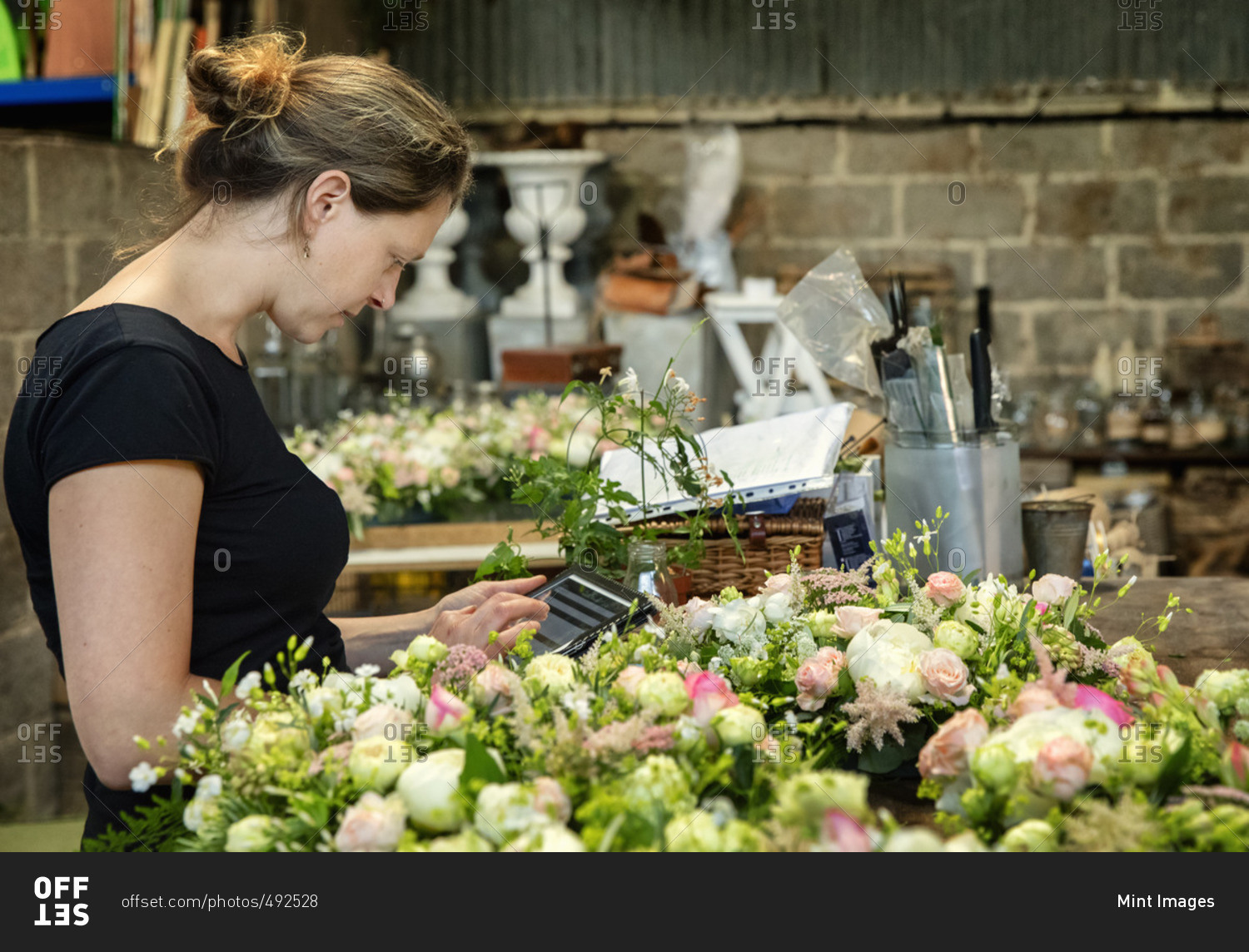 A florist working using a digital tablet by a workench of small flower arrangements.