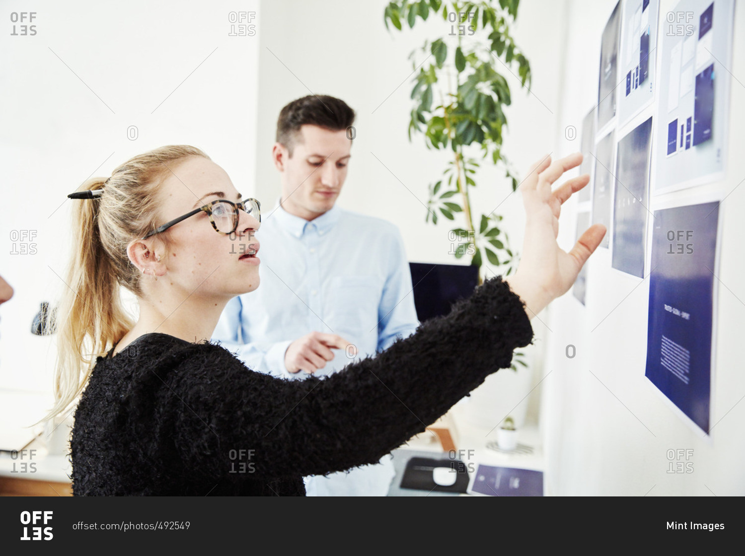 Two people looking at printed plans stuck on a wall, project management and discussions.