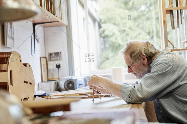 A violin maker at his drawing board drawing out the plans and outline for a new instrument.