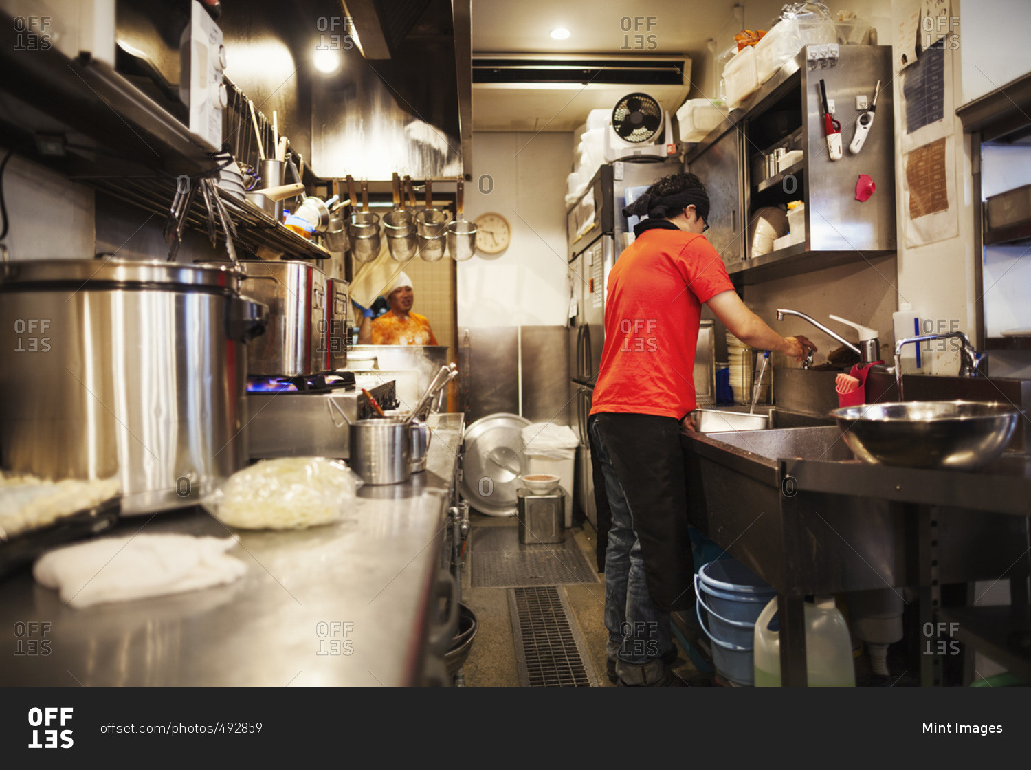Ramen noodle shop. A chef working in a kitchen preparing food using a stove and large pans.