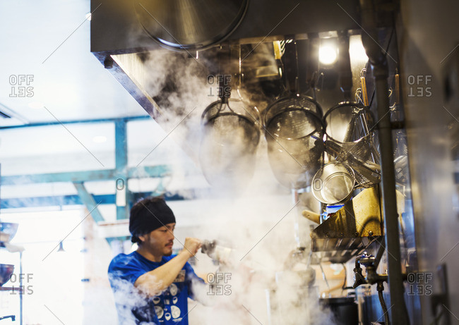 Ramen noodle shop. A chef working in a kitchen with steam rising from the pots of noodles.