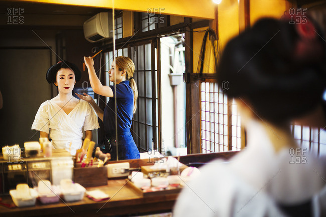 A modern geisha or maiko woman being prepared in traditional fashion, with white face makeup.