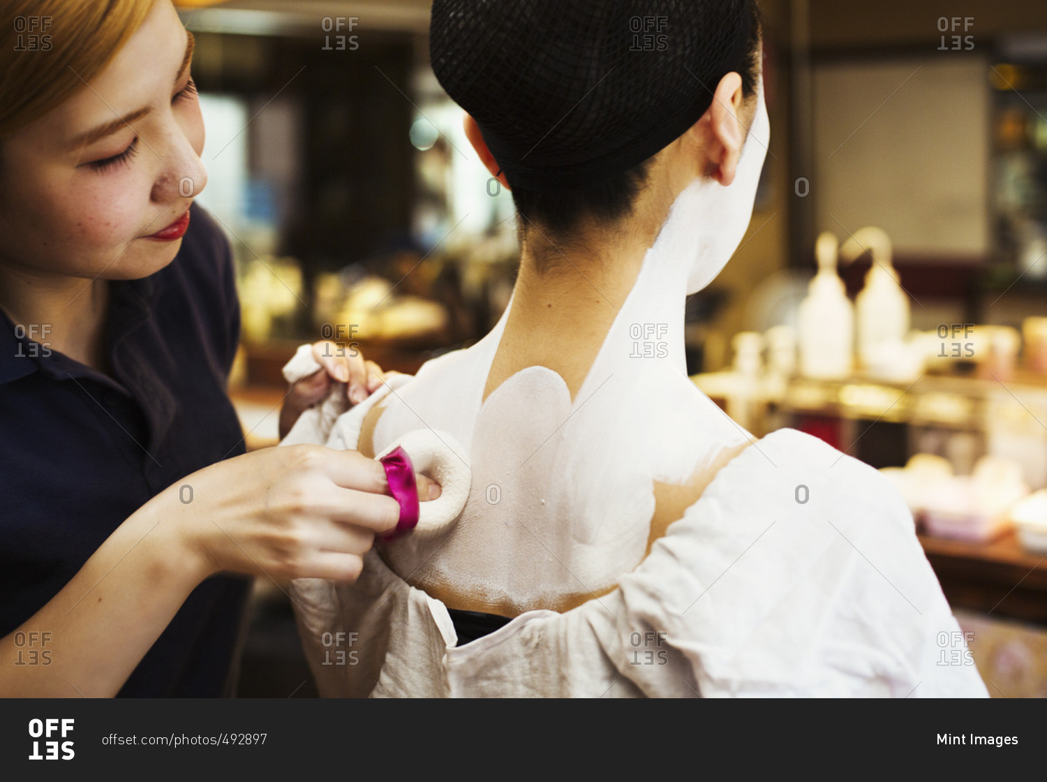 A modern geisha or maiko woman being prepared in traditional fashion, with white face makeup.