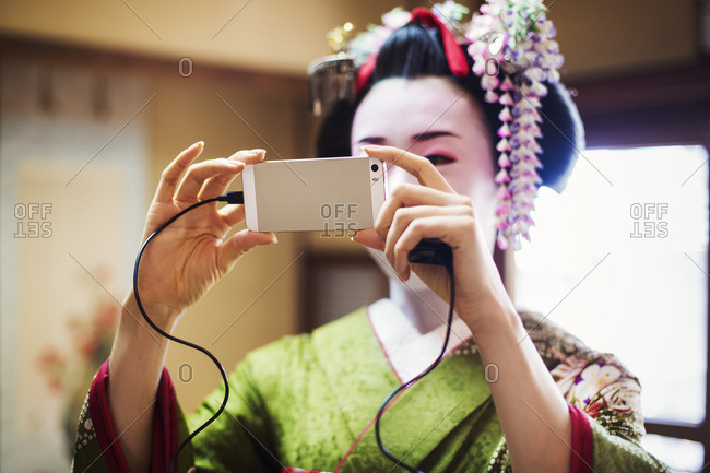 A woman dressed in the traditional geisha style, wearing a kimono and obi, taking a selfie