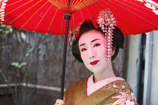 A woman dressed in the traditional geisha style, wearing a kimono with an elaborate hairstyle and floral hair clips