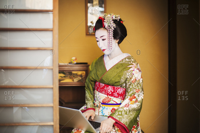 A woman dressed in the traditional geisha style, wearing a kimono and obi using a laptop computer