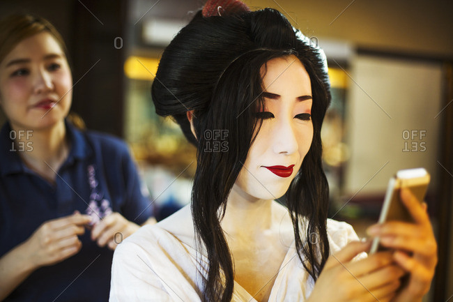 A geisha or maiko with a hair and make up artist creating the traditional hair style and make up.