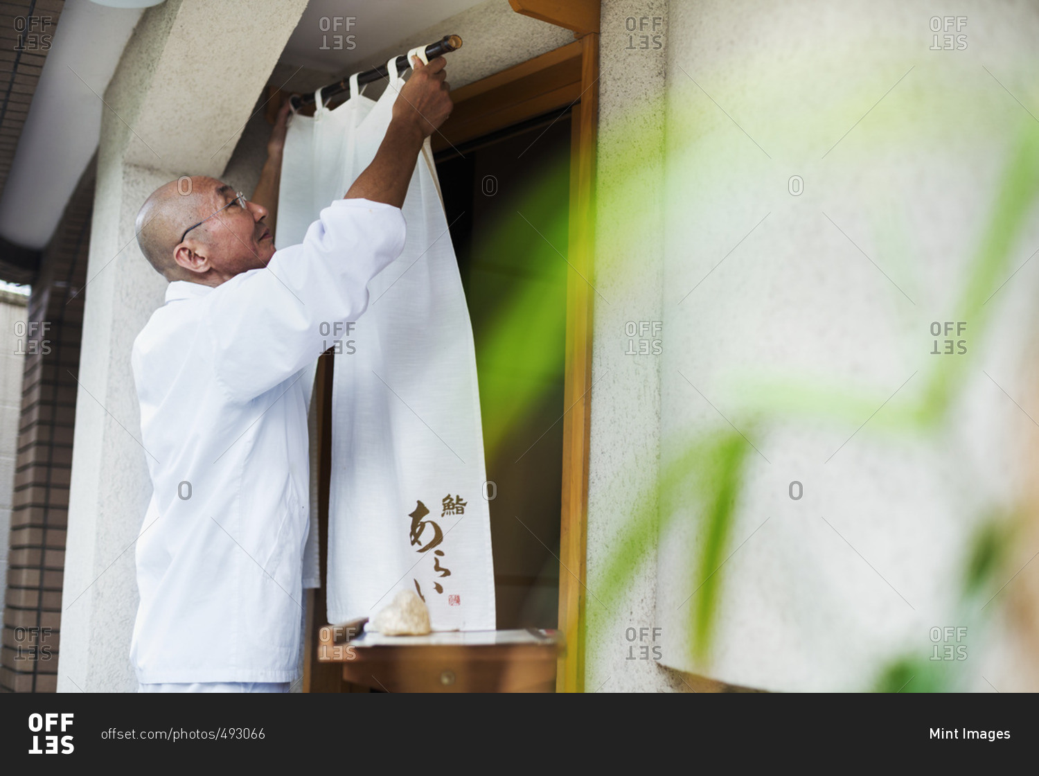 A chef in a small commercial kitchen, an itamae or master chef drawing a curtain across a door.