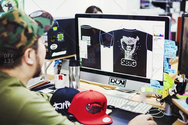 Japan - August 23, 2016: Design Studio. A man seated at a desk using a computer to design tee shirt prints.