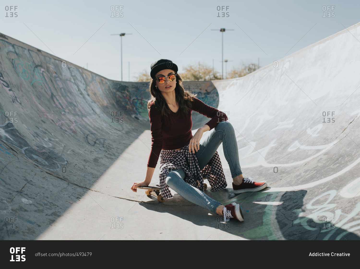 Young female sitting on skateboard in skatepark and looking at camera ...